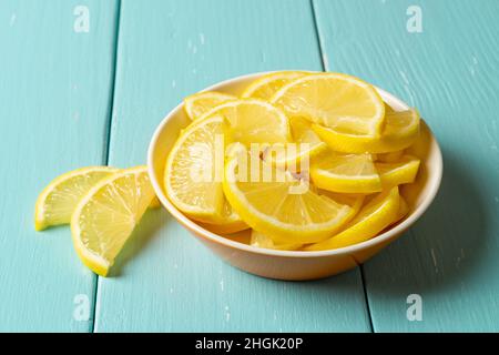 Gros plan de citron juteux frais dans un bol sur une table en bois turquoise.Tranches de citron jaune brut pour antioxydant, saine alimentation, vitamine C concept Banque D'Images