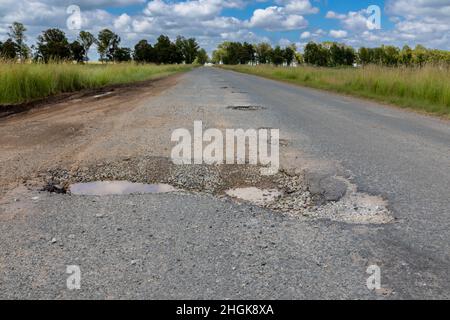 Route asphaltée avec une très grande et profonde cagoule.Le pothole est à moitié rempli d'eau. Banque D'Images