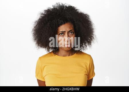 Gros plan sur un portrait d'une femme afro-américaine qui se ternit, qui se met en colère et qui se tient debout dans un t-shirt jaune sur fond blanc Banque D'Images