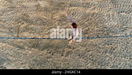 Vue aérienne au-dessus de l'homme en train de desserrer l'équilibrage sur la corde et de faire des acrobaties, démontrant l'agilité, Pacific Beach à San Diego, Californie, États-Unis Banque D'Images