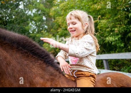 une fille gaie est assise et fait un cheval sur la manie Banque D'Images