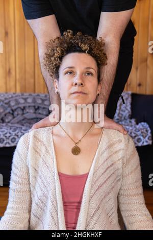 Gros plan portrait d'une femme caucasienne éclairée portant un collier à géométrie sacrée lors d'un massage Shiatsu, les bras de thérapeute travaillent sur les épaules. Banque D'Images