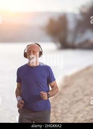 Homme senior en vêtements de fitness avec écouteurs le long de la plage Banque D'Images