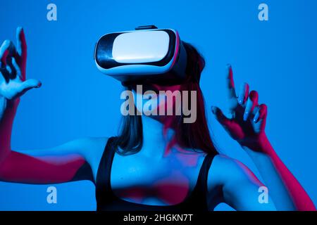 Une jeune femme stupéfait de toucher l'air pendant l'expérience VR.Fille utilise un casque de réalité virtuelle dans la lumière de néon.La femme avec des lunettes de virtuel Banque D'Images