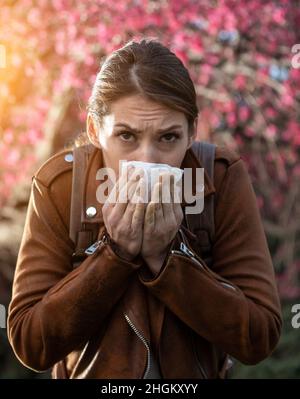 Jeune jolie fille soufflant le nez devant l'arbre en fleur. Réaction allergique printanière Banque D'Images