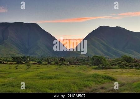 Des nuages enflammés tandis que le soleil se lève sur les montagnes de maui à l'ouest. Banque D'Images