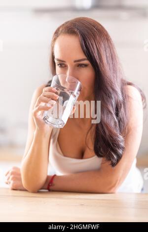 Femme en chemise blanche boit un verre d'eau douce pour se réhydrater. Banque D'Images