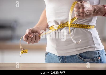 Détail d'une femme serrant le ruban de mesure autour de sa taille dans un effort de perdre du poids. Banque D'Images