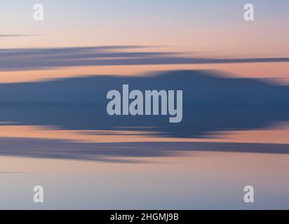 Mouvement intentionnel de la caméra coucher du soleil paysage image de montagnes lointaines avec des couleurs pastel reflétées dans l'océan calme Banque D'Images