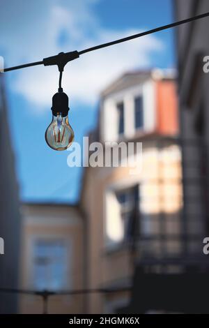 Une ampoule électrique est suspendue sur un fil contre un ciel bleu dans l'ancienne ville de Riga.Anciens bâtiments d'architecture intéressante dans les rues de Banque D'Images