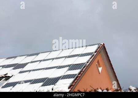 Le toit carrelé de la maison avec panneaux solaires est recouvert de neige en hiver. Banque D'Images