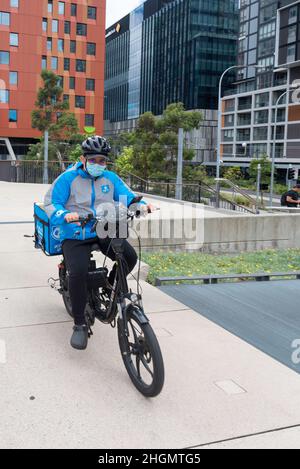 Un pilote de livraison sur un vélo alimenté par batterie portant un casque et un masque covid, se déplace sur la ligne des marchandises à Sydney, Nouvelle-Galles du Sud, Australie Banque D'Images