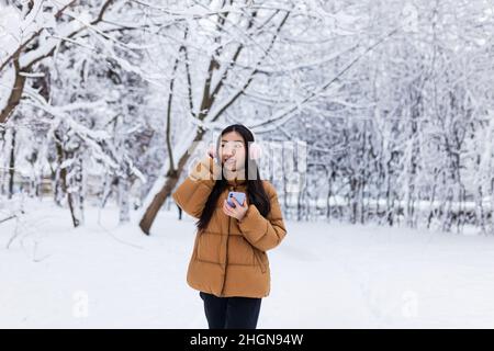 De belles promenades d'adolescents japonais dans le parc d'hiver utilisent le téléphone et écoute de la musique avec de jolis casques roses Banque D'Images