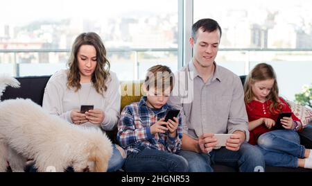 Les membres de la famille sont charmants et passent du temps à jouer avec leur smartphone Banque D'Images