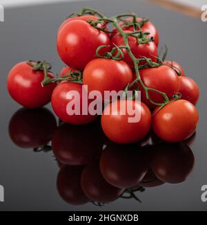 Belles tomates de vigne fraîches (cerise) avec des gouttes d'eau, brutes, entières et coupées en deux. Sur fond d'ardoise texturé noir. Ingrédients de la Méditerranée Banque D'Images