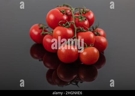 Belles tomates de vigne fraîches (cerise) avec des gouttes d'eau, brutes, entières et coupées en deux. Sur fond d'ardoise texturé noir. Ingrédients de la Méditerranée Banque D'Images