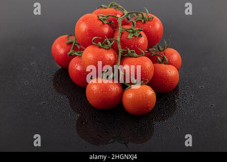 Belles tomates de vigne fraîches (cerise) avec des gouttes d'eau, brutes, entières et coupées en deux. Sur fond d'ardoise texturé noir. Ingrédients de la Méditerranée Banque D'Images
