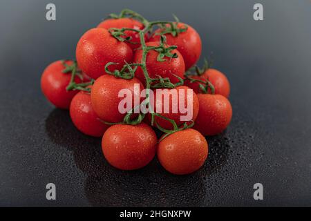 Belles tomates de vigne fraîches (cerise) avec des gouttes d'eau, brutes, entières et coupées en deux. Sur fond d'ardoise texturé noir. Ingrédients de la Méditerranée Banque D'Images