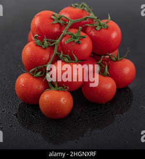 Belles tomates de vigne fraîches (cerise) avec des gouttes d'eau, brutes, entières et coupées en deux. Sur fond d'ardoise texturé noir. Ingrédients de la Méditerranée Banque D'Images