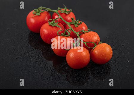 Belles tomates de vigne fraîches (cerise) avec des gouttes d'eau, brutes, entières et coupées en deux. Sur fond d'ardoise texturé noir. Ingrédients de la Méditerranée Banque D'Images