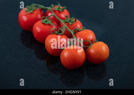 Belles tomates de vigne fraîches (cerise) avec des gouttes d'eau, brutes, entières et coupées en deux. Sur fond d'ardoise texturé noir. Ingrédients de la Méditerranée Banque D'Images