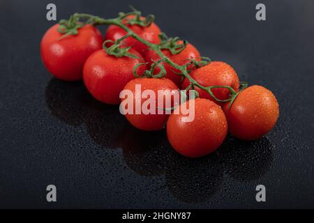 Belles tomates de vigne fraîches (cerise) avec des gouttes d'eau, brutes, entières et coupées en deux. Sur fond d'ardoise texturé noir. Ingrédients de la Méditerranée Banque D'Images