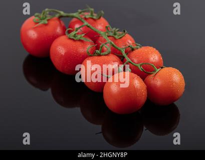 Belles tomates de vigne fraîches (cerise) avec des gouttes d'eau, brutes, entières et coupées en deux. Sur fond d'ardoise texturé noir. Ingrédients de la Méditerranée Banque D'Images