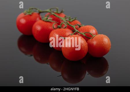 Belles tomates de vigne fraîches (cerise) avec des gouttes d'eau, brutes, entières et coupées en deux. Sur fond d'ardoise texturé noir. Ingrédients de la Méditerranée Banque D'Images