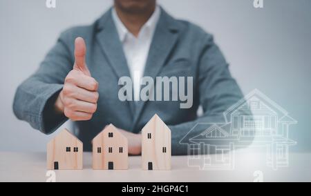 Homme d'affaires montrant les pouces vers le haut mini et modèle de maison en bois du modèle sur table en bois, planification achat Immobilier, planification pour acheter la propriété. Concept Banque D'Images