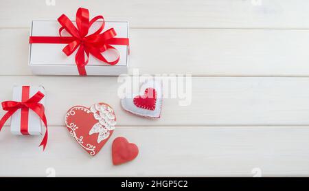 Arrière-plan avec des bonbons au pain d'épice sous forme de coeurs avec des cadeaux pour la Saint-Valentin avec un espace de copie sur une table en bois blanc. Banque D'Images