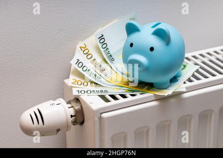 Billets de 100 et 200 euros couchés sur le radiateur avec une petite banque de porc bleue, le concept de la hausse des coûts de chauffage d'un appartement en Europe Banque D'Images