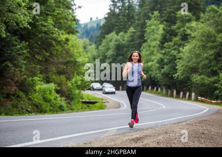 Femme de course sur la route de montagne à travers la forêt. Banque D'Images