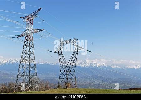 Pylônes électriques dans un paysage de campagne avec des montagnes enneigées en arrière-plan Banque D'Images