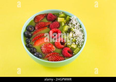 bol à smoothie avec baies fraîches et fruits dans une assiette bleue sur jaune Banque D'Images