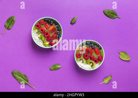 bol à smoothie avec baies fraîches et fruits dans une assiette bleue sur violet avec feuilles d'épinards Banque D'Images