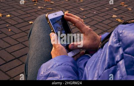 Une femme tient un téléphone portable dans ses mains contre le fond des feuilles d'automne éparpillées sur le trottoir. Banque D'Images