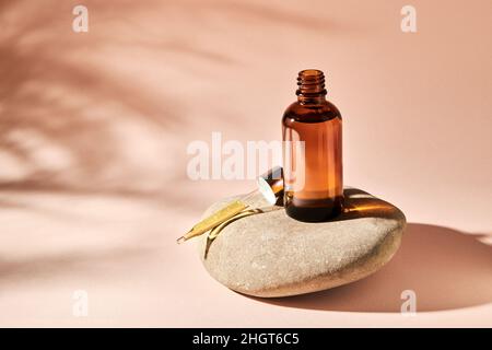 Huile essentielle sur une pierre de galet de rivière sur un fond beige.Produit de beauté médical cosmétique en bouteille de verre brun avec une pipette pour l'aromathérapie, Banque D'Images