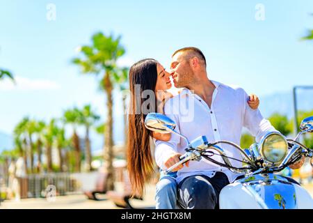 Beau jeune couple amoureux à cheval sur un scooter dans une belle plage de bord de mer à la journée de synny Banque D'Images