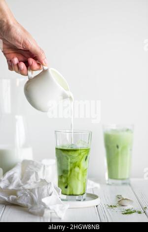 Latte glacé au matcha et au lait d'amande faits maison sur fond de béton léger.Femme versez le lait dans le verre avec du matcha latte. Banque D'Images
