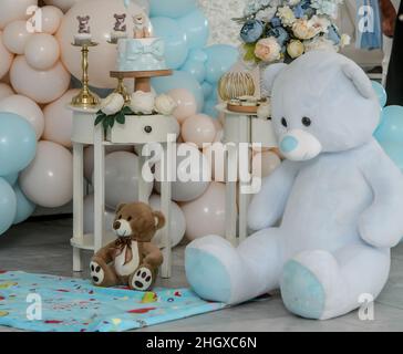 L'ours en peluche se trouve sur le fond avec différentes couleurs de ballons, guirlande d'anniversaire, fleurs bleues et blanches.Célébrer la première année de vie de bébé.Décoration Banque D'Images