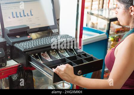 latina femme regardant déçu à la caisse de son entreprise pour voir combien d'argent il y a. fille travaillant dans le quartier latino-américain sto Banque D'Images