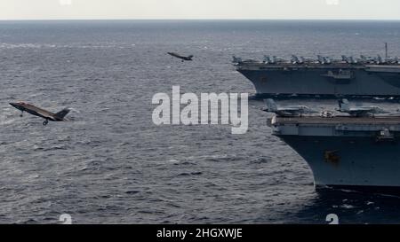 220122-N-PQ495-1208 MER DES PHILIPPINES (JANV22, 2022) un F-35C Lightning II, affecté aux “Argonautes” de l’Escadron de combat Strike (VFA) 147, sort du pont de vol du porte-avions de la classe Nimitz USS Carl Vinson (CVN 70), tandis qu’un F-35C Lightning II, affecté au “Black Knights” Marine Strike Fighter Squadron (VMFA) 314,Lance le pont de vol du porte-avions de la classe Nimitz USS Abraham Lincoln (CVN 72) le 22 janvier 2022.Faisant partie de la flotte du Pacifique des États-Unis, des unités sont attribuées aux groupes de grève des transporteurs Carl Vinson et Abraham Lincoln, aux groupes prêts à l'emploi amphibie d'Essex et d'Amérique et au Jap Banque D'Images