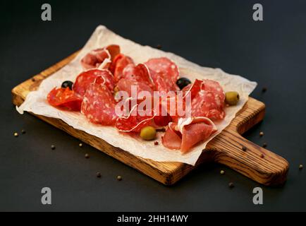 coupes froides - jamon, jambon, salami sur un panneau en bois sur fond noir Banque D'Images