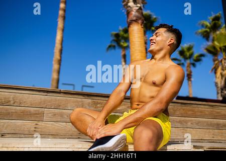 latino-homme appliquant une lotion de bronzage à la mer avec un fond de palmiers Banque D'Images