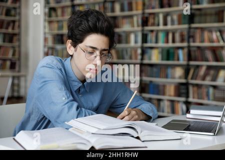 Un élève sérieux du secondaire travaillant sur un projet de remise des diplômes à la bibliothèque Banque D'Images