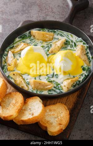 Les œufs traditionnels de la Nouvelle-Orléans, sardou, crème d'épinards, artichauts, œufs pochés et sauce hollandaise, se trouvent dans l'assiette de la table.Verticale Banque D'Images