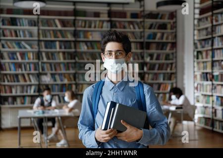 Étudiant de fraîcheur en masque de protection médical et sac à dos visitant la bibliothèque Banque D'Images