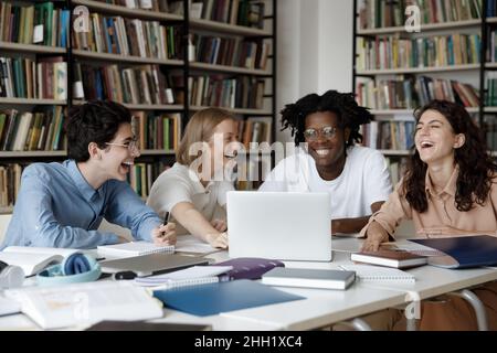 Joyeux et joyeux étudiants diplômés divers coopérant à la bibliothèque de l'université Banque D'Images