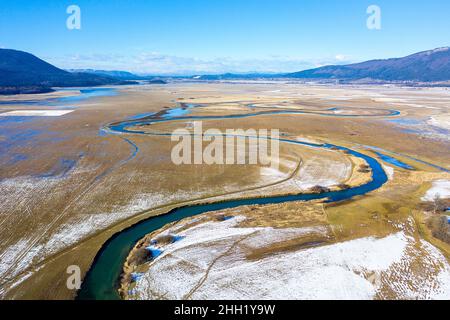 Vue aérienne de dessus de affluent qui coule dans le lac Cerknica, belle vue sur le lac gelé intermittent et les montagnes, prise par drone, Slovénie Banque D'Images