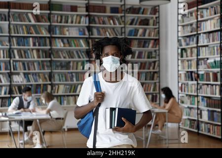 Étudiant africain de sexe masculin portant un masque de protection du visage, visitant la bibliothèque de l'université Banque D'Images